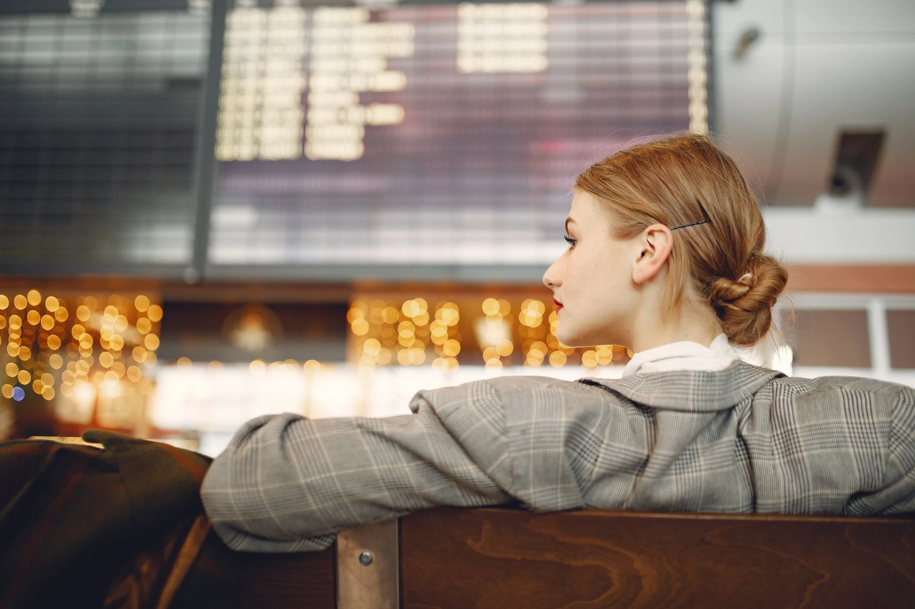 Painel de partidas desfocado e viajante à espera num aeroporto