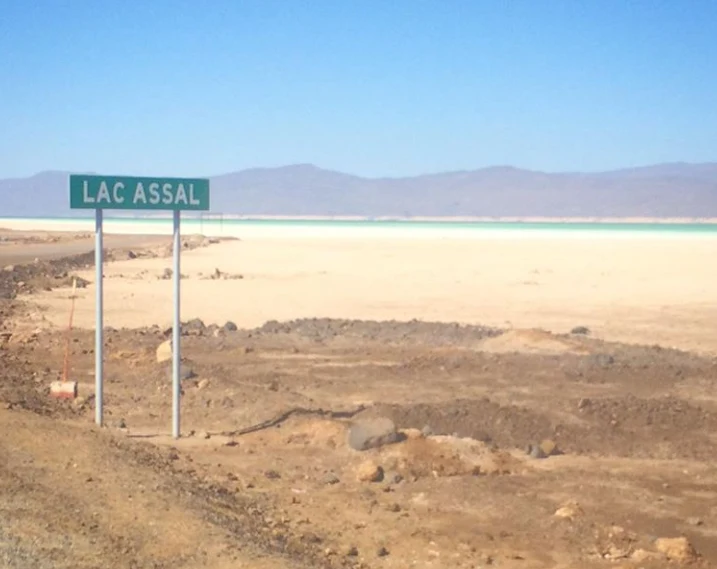 Carretera asfaltada hacia el lago Assal entre lava negra y paisaje árido.