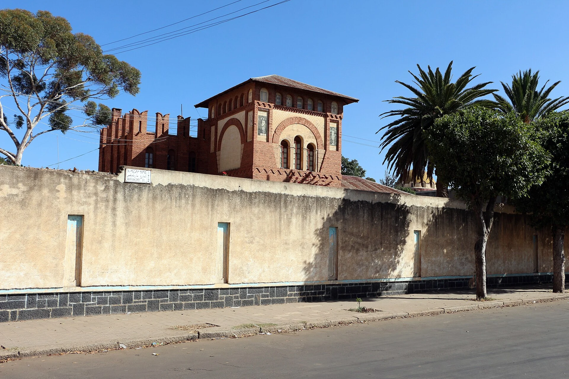 Calle de Asmara con comercios de barrio y siluetas religiosas al fondo.