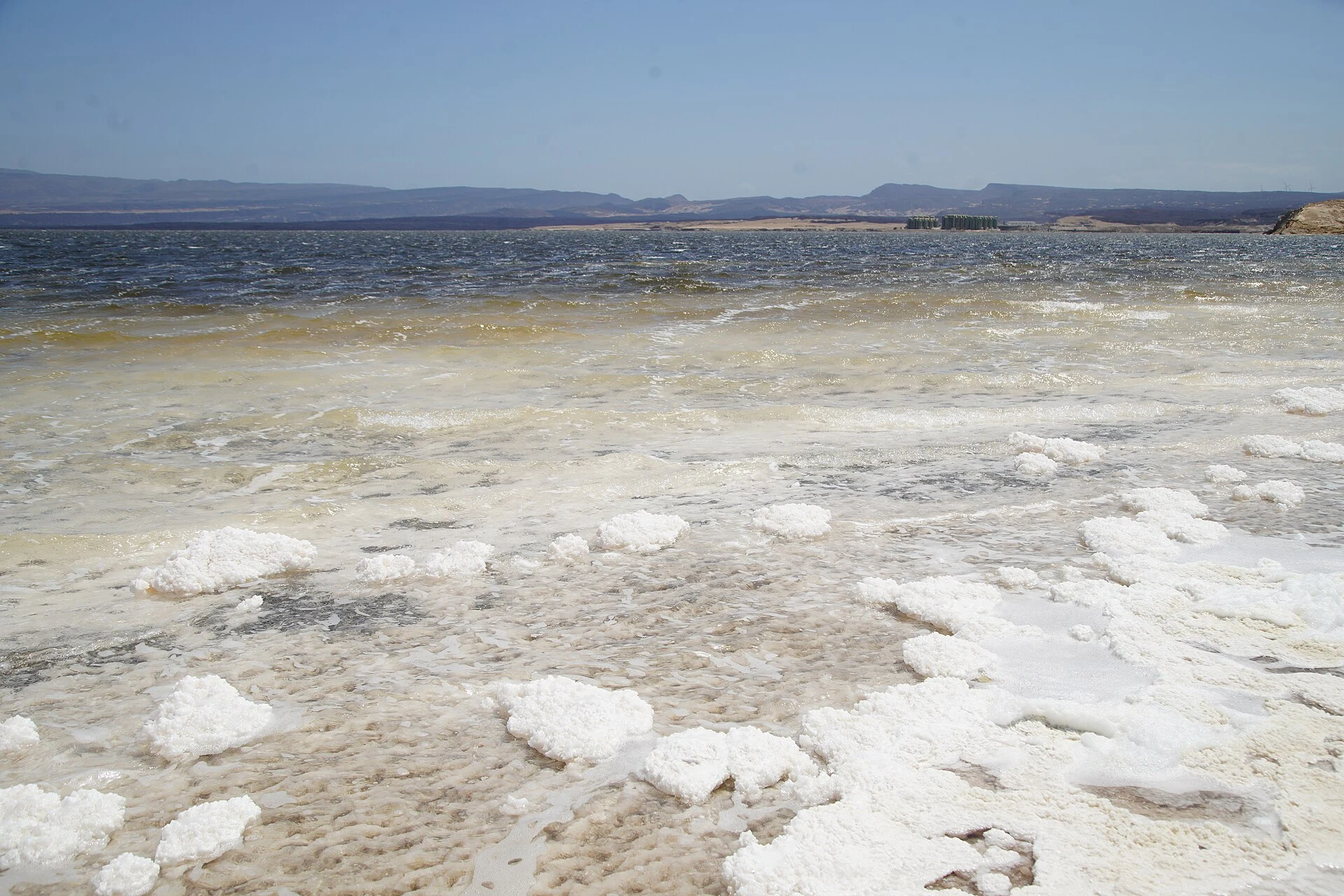 Vista amplia del Lago Assal con costras de sal, agua turquesa y montañas volcánicas.