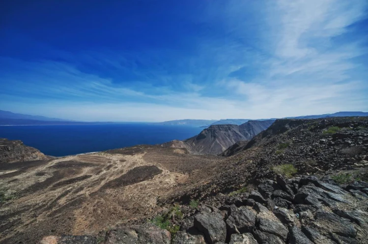 Panorámica de Ghoubbet al-Kharab con costa volcánica oscura e Isla del Diablo.
