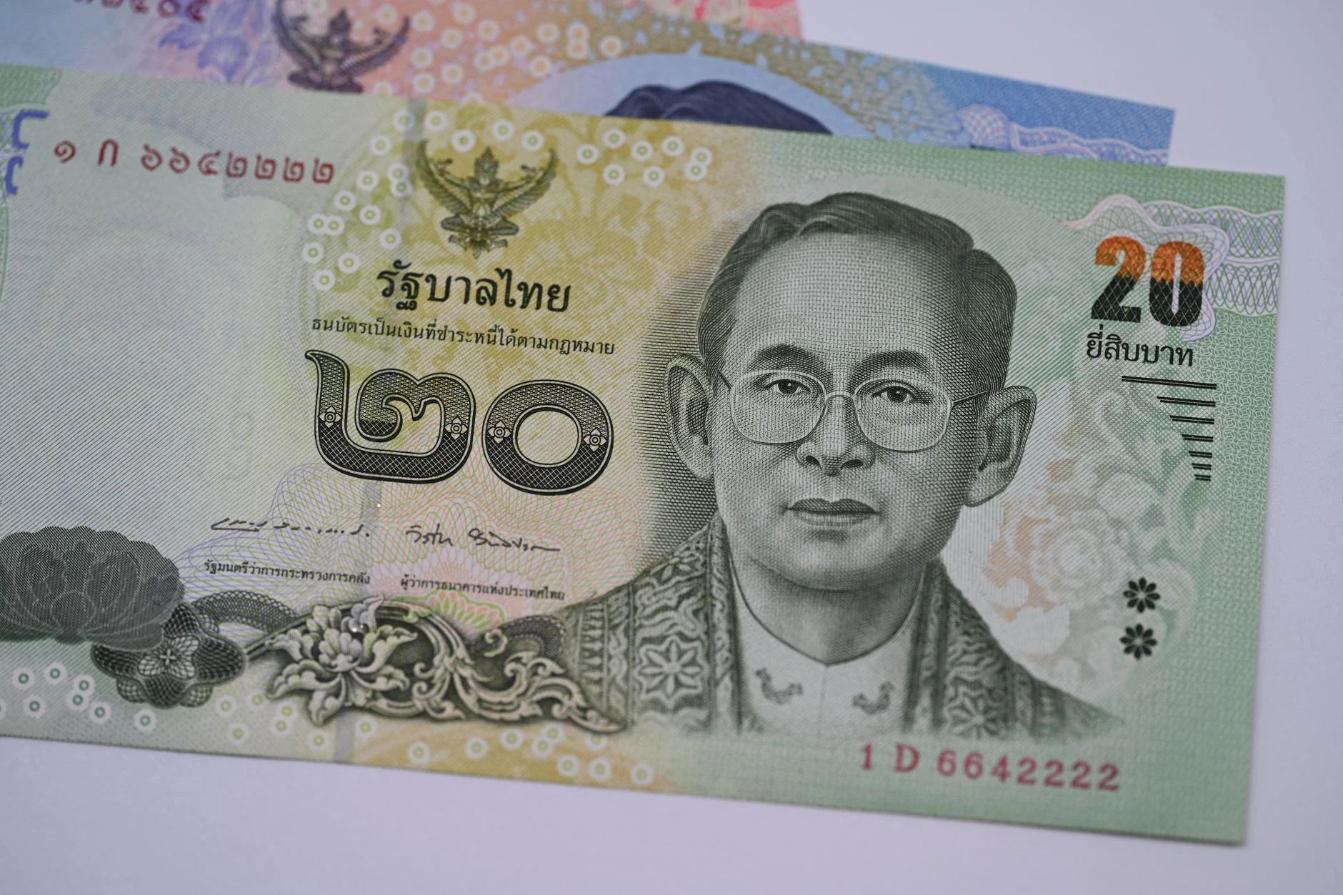 Billetes de baht tailandés junto a texto en tailandés, como referencias nacionales.